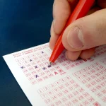 A hand filling in the numbers on a paper lottery ticket