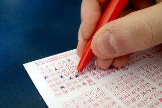 A hand filling in the numbers on a paper lottery ticket