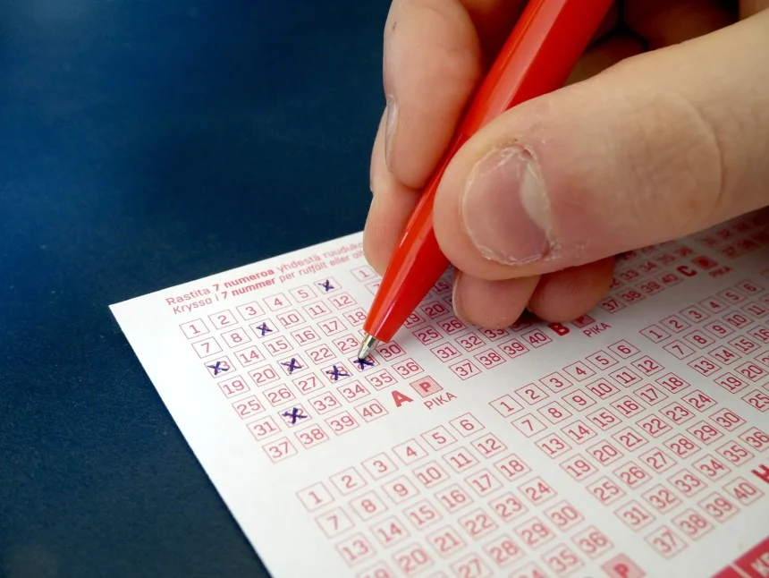 A hand filling in the numbers on a paper lottery ticket